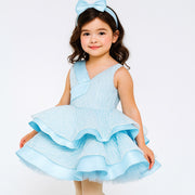 Young girl wearing a light blue dress with ruffles on a white background