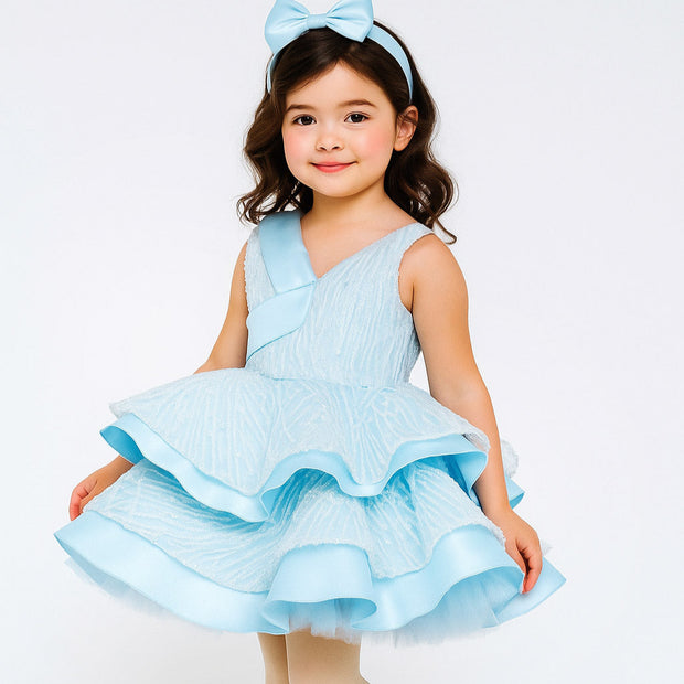 Young girl wearing a light blue dress with ruffles on a white background