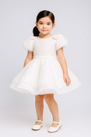 Young girl wearing a ivory dress with fluffy sleeves against a plain background