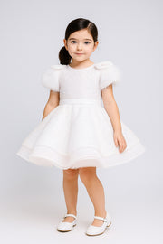 Young girl wearing a white dress with puffed sleeves against a white background